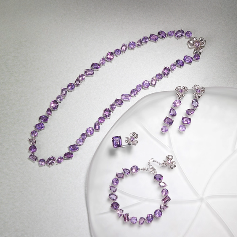 Silver-toned amethyst jewelry set (necklace, ring, bracelet, earrings) with mixed-cut purple gemstones and flower-shaped accents. Cohesive, vibrant design ideal for formal events or gifting.