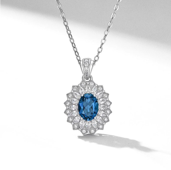 Silver-toned necklace with an oval-cut vibrant blue topaz pendant, framed by diamond clusters (floral style). Dainty chain, bright and elegant for gifting or daily wear.