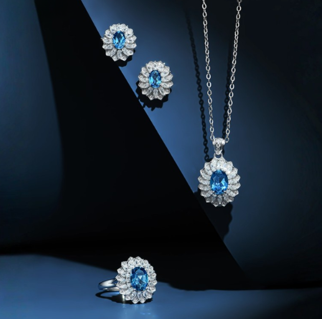 Silver-toned topaz and diamond jewelry set (necklace, ring, earrings)—features oval-cut vibrant blue topaz surrounded by brilliant-cut diamonds (floral setting). Crisp, elegant design ideal for special occasions.