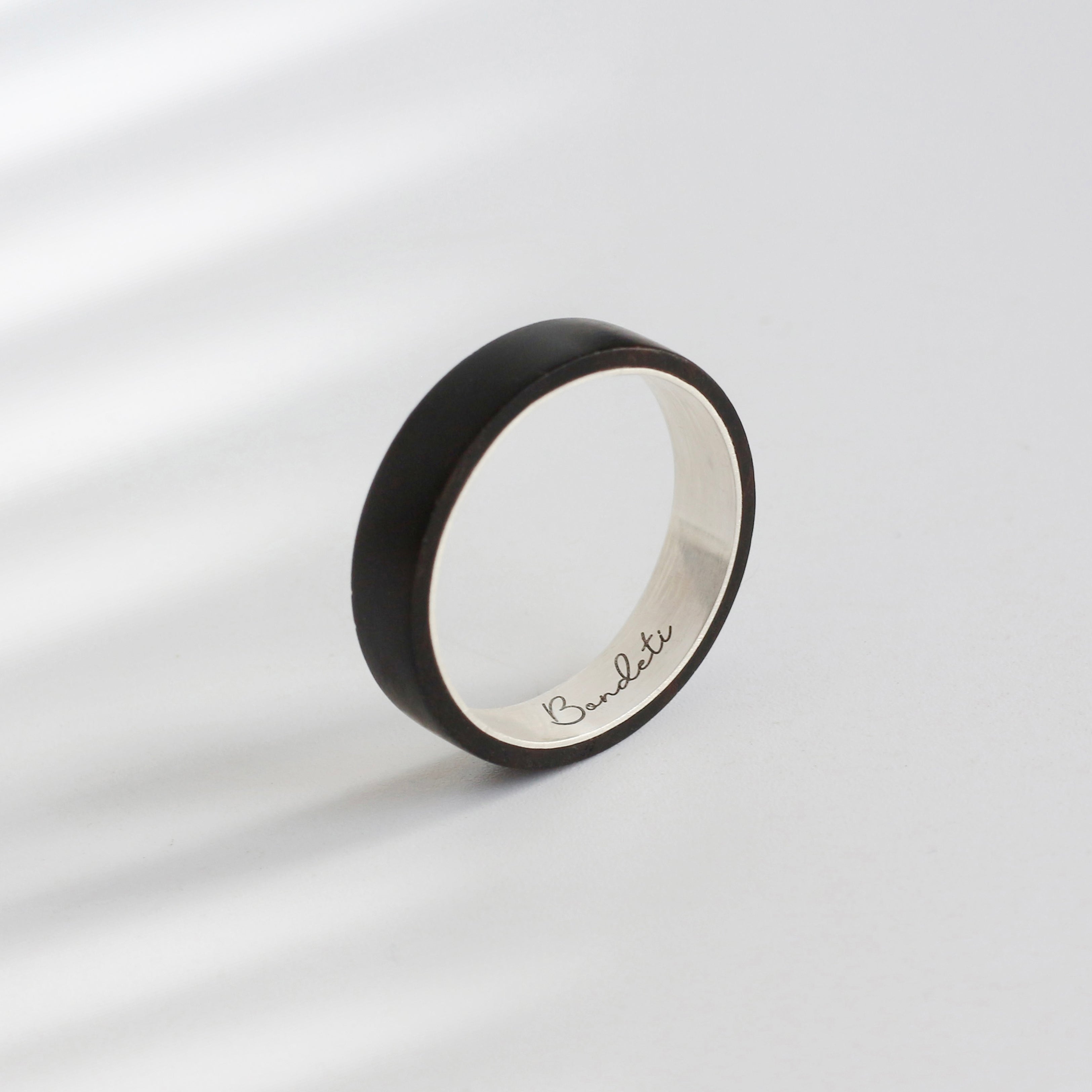 A sleek black ebony silver ring with a polished silver interior. Custom - made, it features the name "Bandetti" engraved inside. Perfect as a unique wooden wedding gift, combining elegance and personalization.