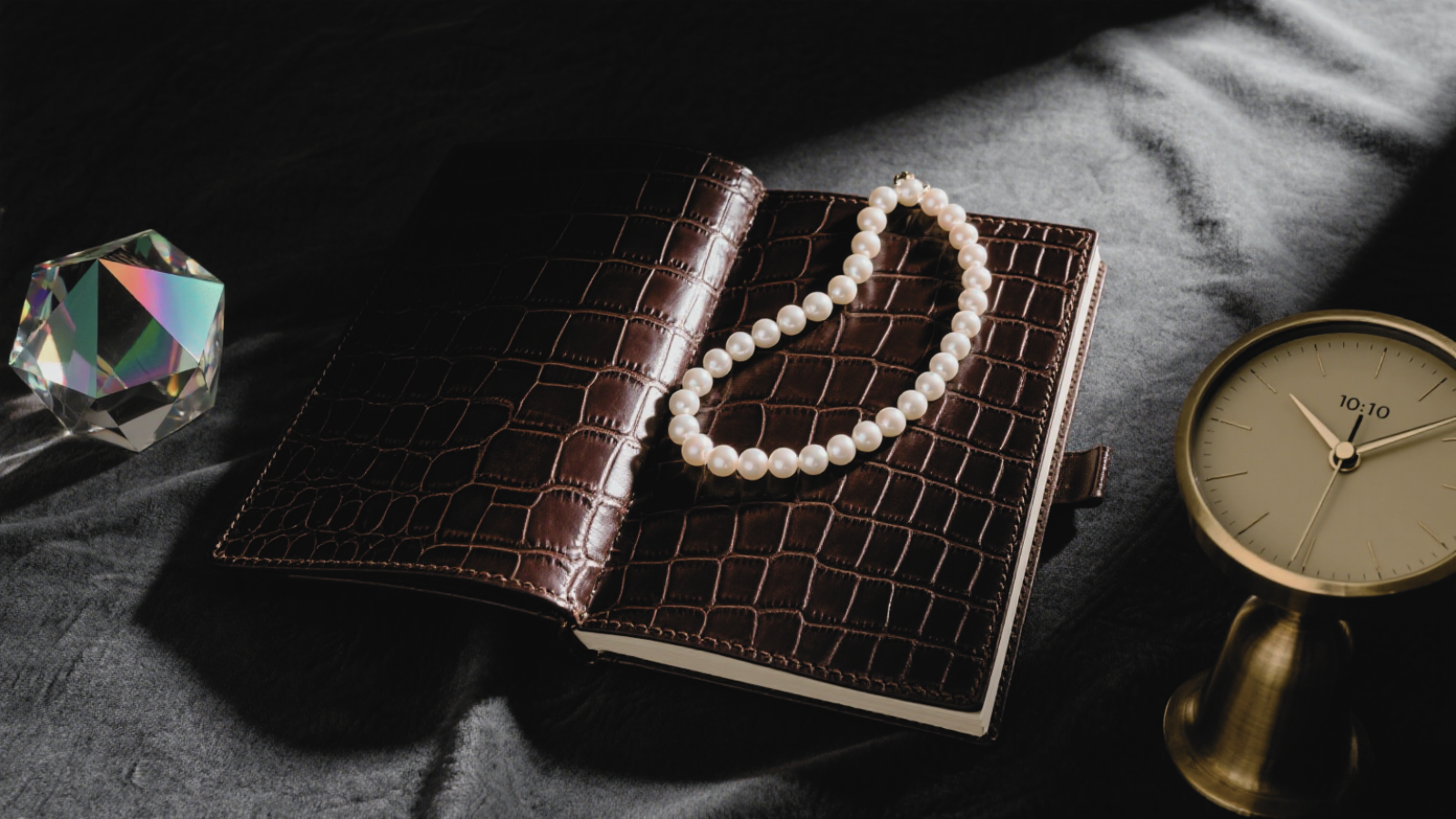 A crocodile - patterned notebook, a classic pearl necklace, and an iridescent crystal, paired with a minimalist clock. Perfect for couples to record shared memories, a timeless anniversary gift. 