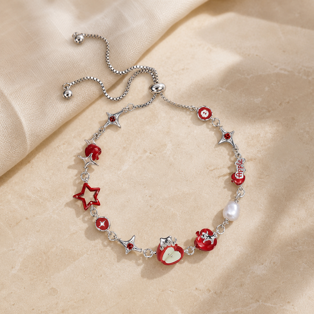 Silver adjustable bracelet with red apple, star and pearl charms arranged on warm beige stone