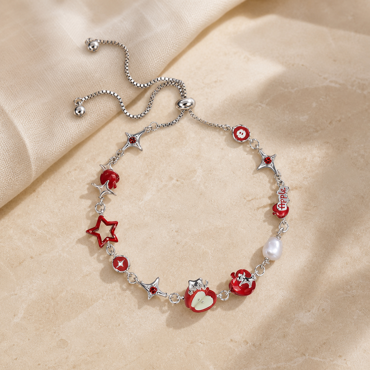 Silver adjustable bracelet with red apple, star and pearl charms arranged on warm beige stone