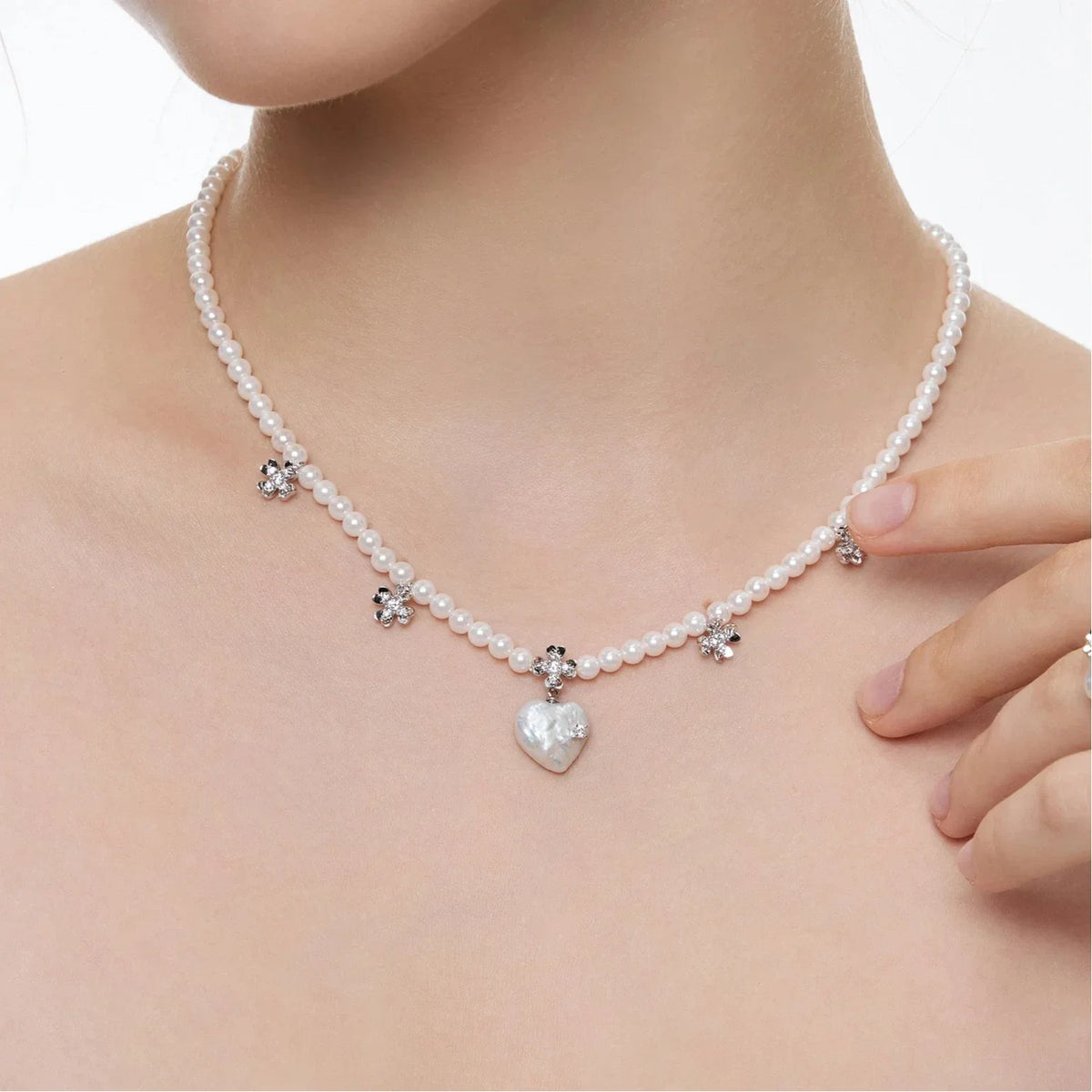 Pearl Heart Necklace with Floral Stations — close neckline-worn view with fingers near the floral stations