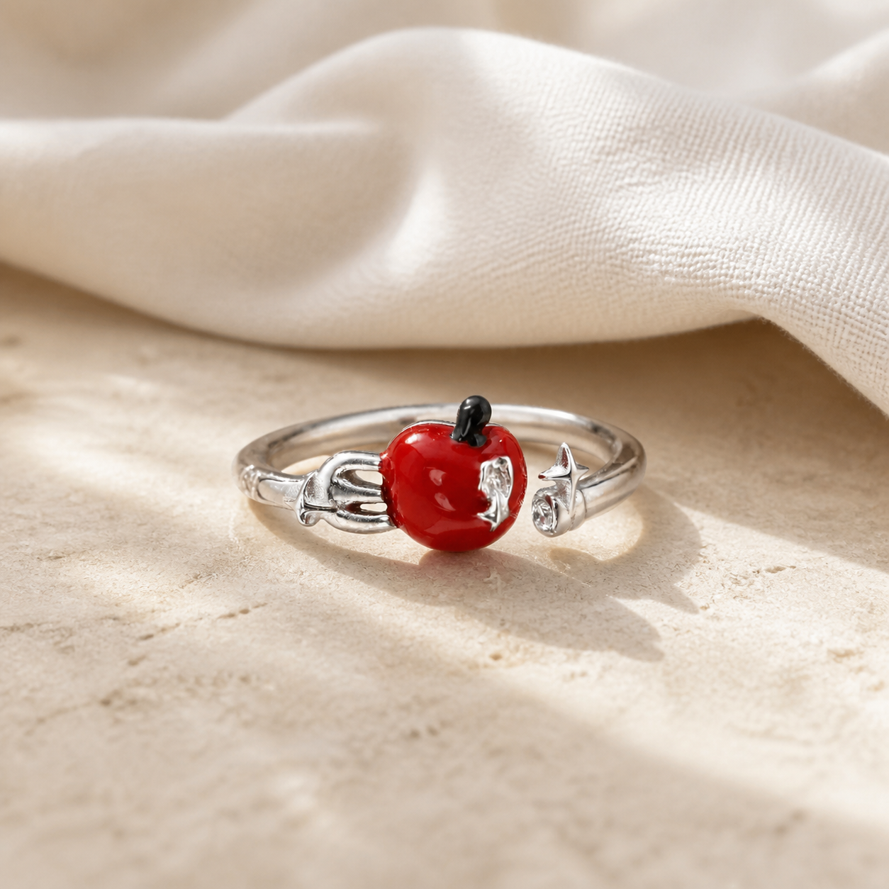 Silver open ring with a glossy bitten red apple and star accent displayed on warm beige stone