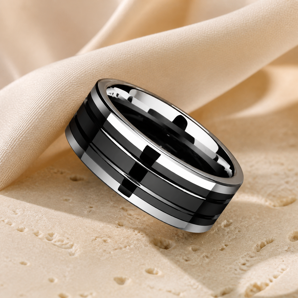 Glossy black ceramic tungsten ring with silver-tone horizontal bands displayed on warm beige stone