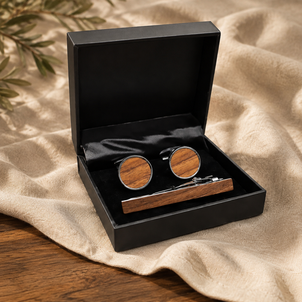 Black walnut cufflinks and matching tie clip in a black gift box on warm linen