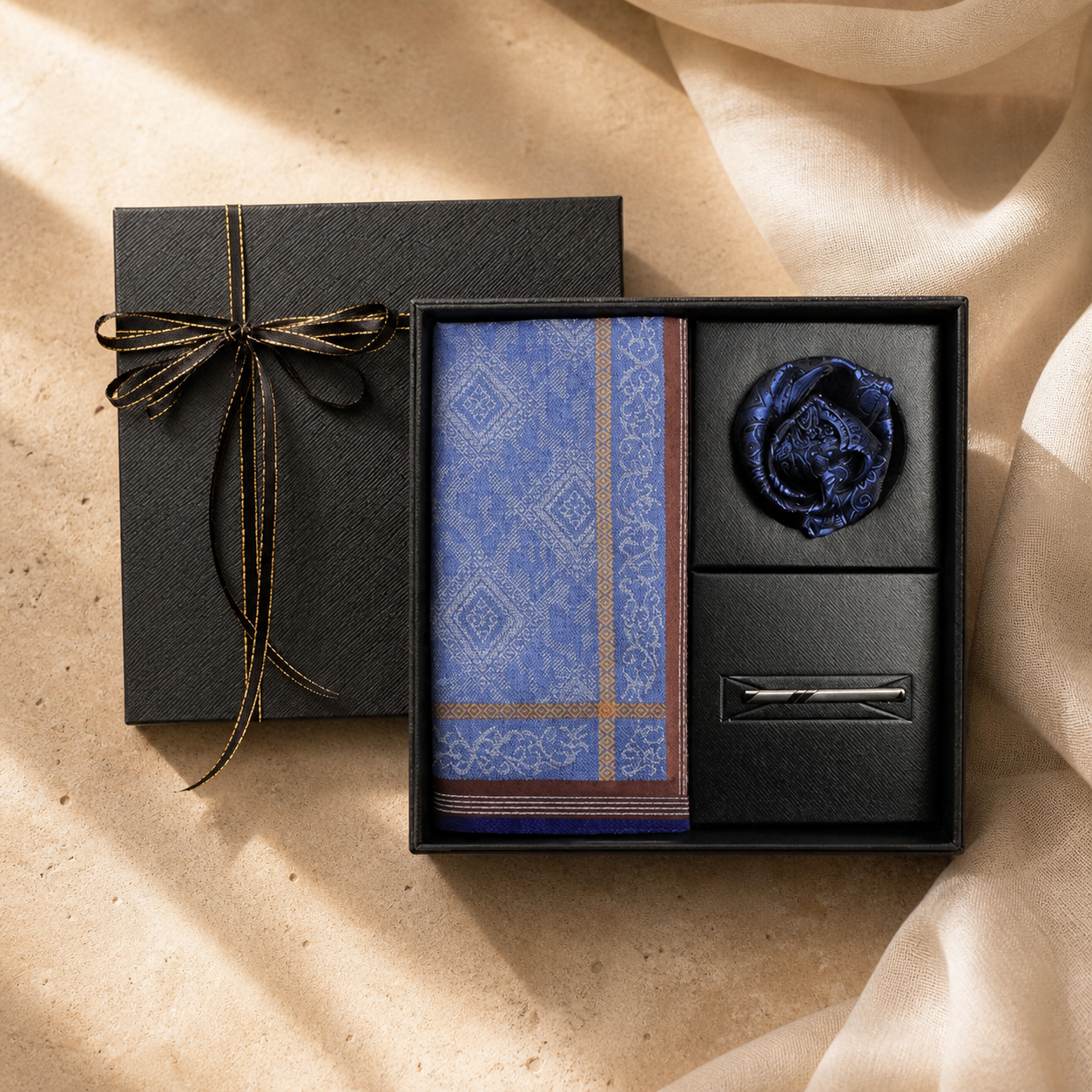 Open black gift box with a blue patterned cotton handkerchief, wax seal and silver accessory