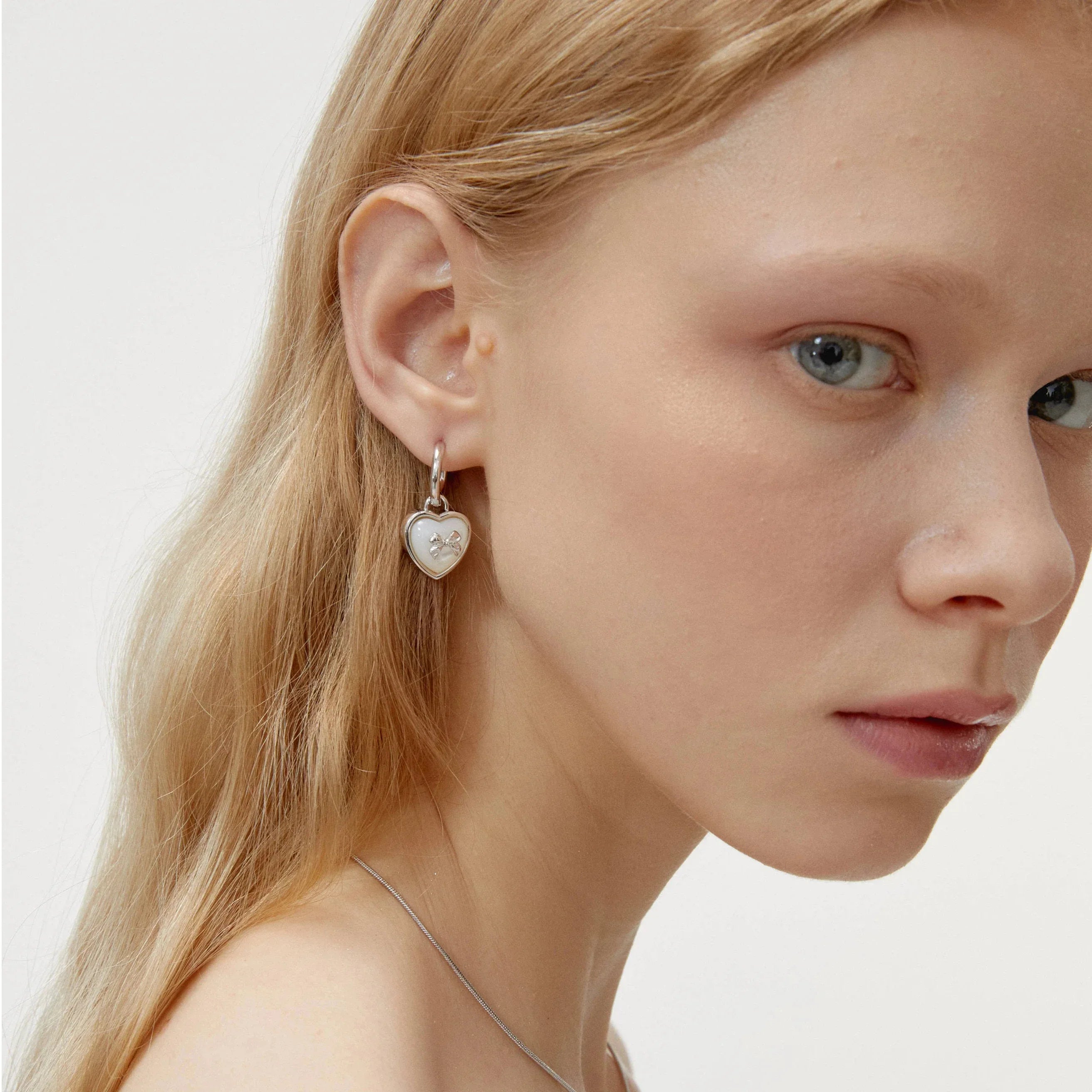 Pearl Heart Drop Earrings with Bow Detail — right-ear worn portrait showing the heart-drop scale