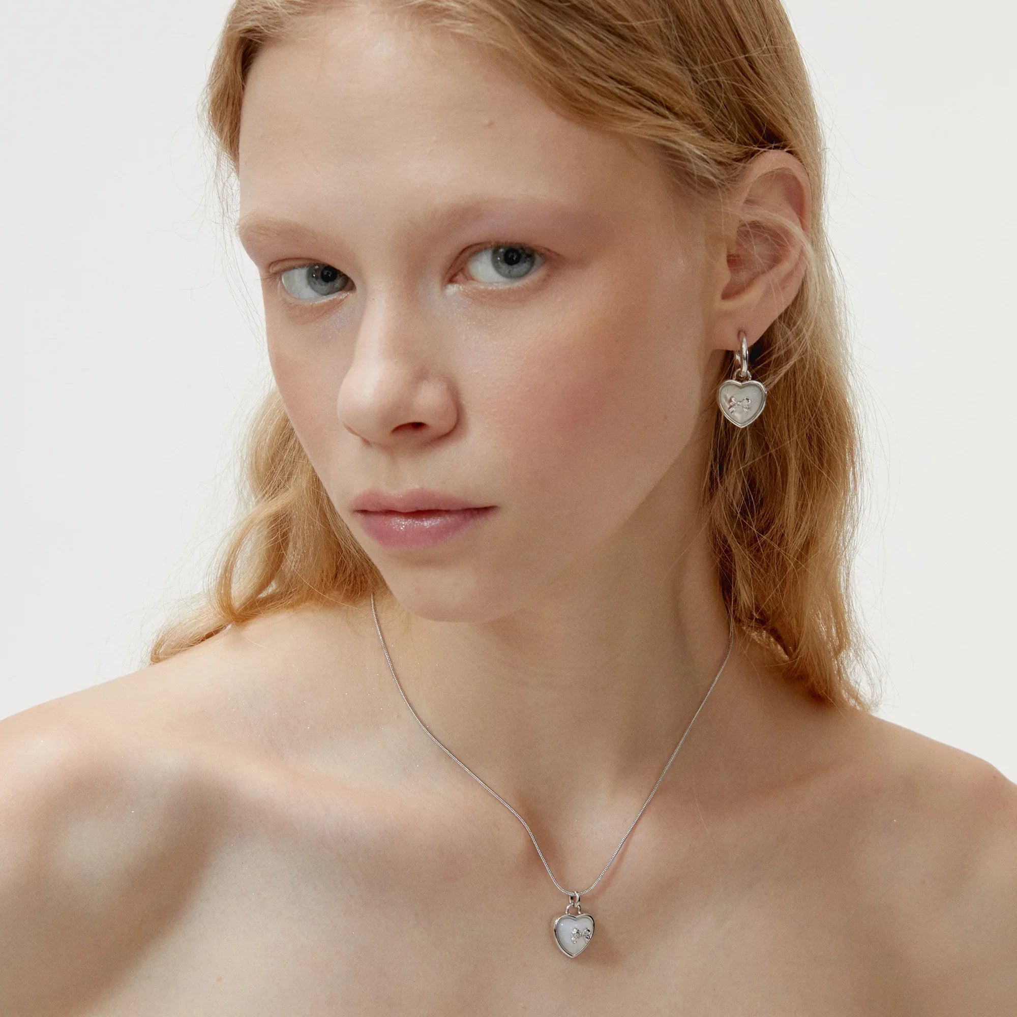 Pearl Heart Drop Earrings with Bow Detail — front model portrait wearing the earrings with a matching heart necklace