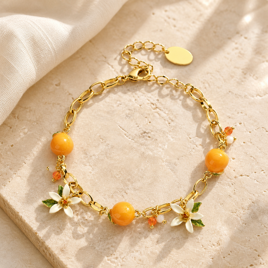 Gold bracelet with three orange citrus charms, white blossoms and green leaves on beige stone