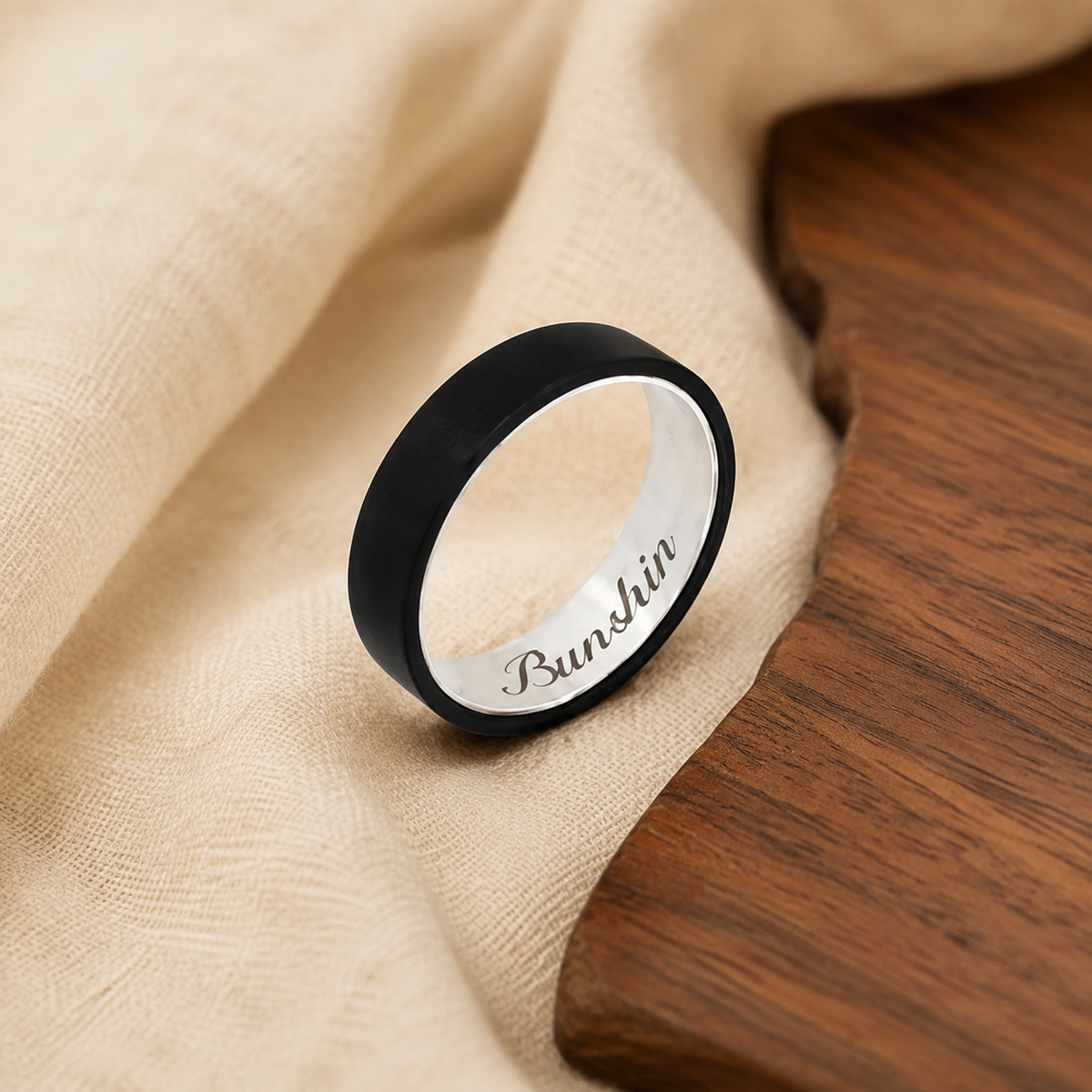 Customized black ebony and silver ring on warm linen beside natural wood