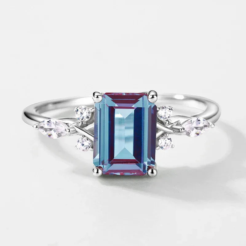 Emerald-cut Alexandrite ring with leaf side accents, center stone close-up on a white background