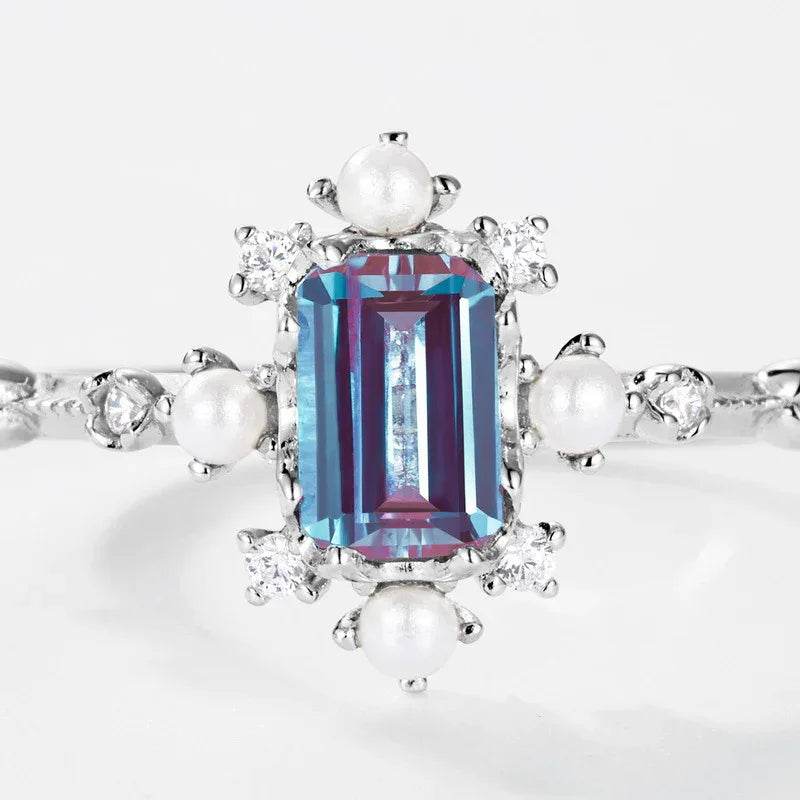 Emerald-cut Alexandrite ring with pearl and clear accents, center stone close-up on a white background