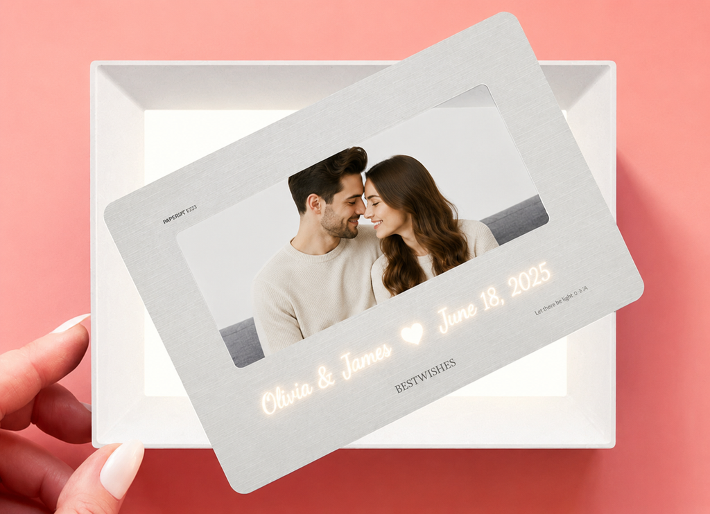 Hand holding personalized hidden message film card showing translucent paper film card with couple photo and glowing script names Olivia and James heart June 18 2025 in warm LED light above white LED light frame base on pink background