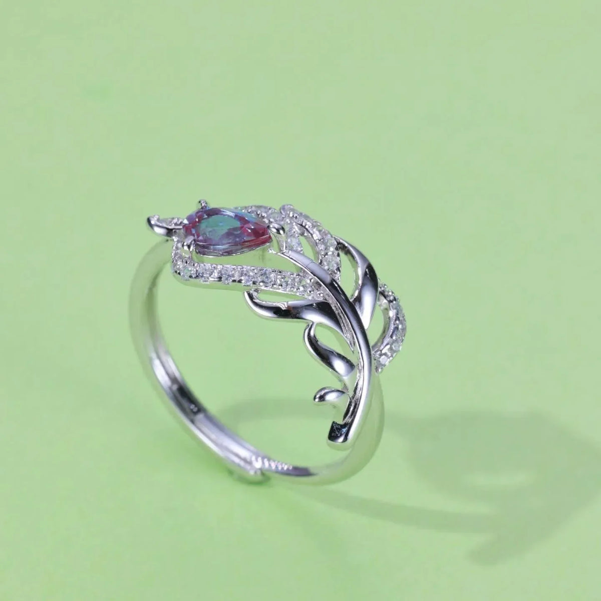 Feather-wrap ring with a Alexandrite and clear accents, angled product view on a colored background