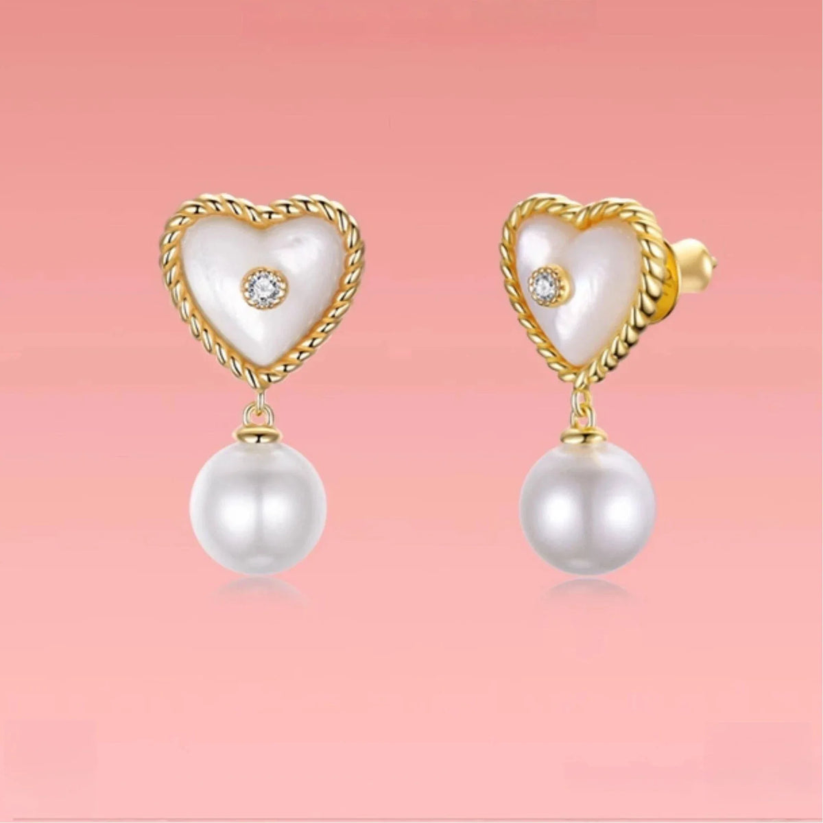 Pearl Drop Heart Earrings with Clear Center Accents — pair displayed on a pink background