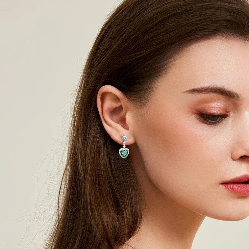 Heart-Cut Emerald Drop Earrings worn on the ear in a close-up
