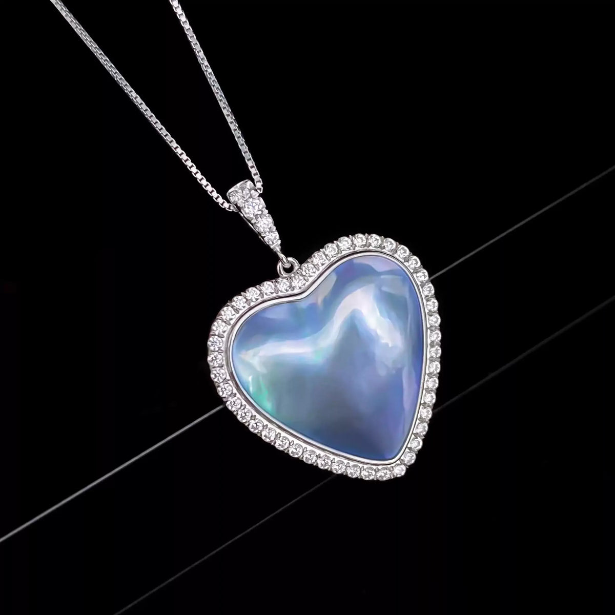 Blue Iridescent Pearl Heart Halo Pendant Necklace — macro pendant view on a black background showing the clear halo