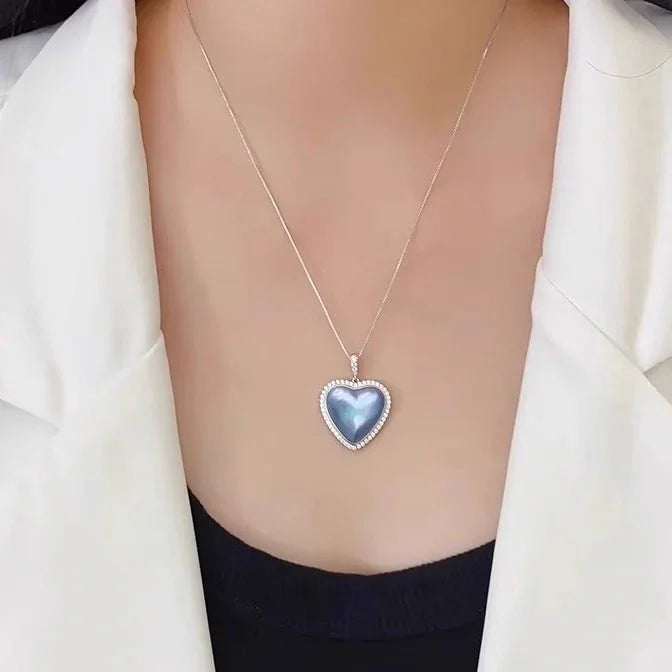 Blue Iridescent Pearl Heart Halo Pendant Necklace — chest-worn view over a white blazer and black top
