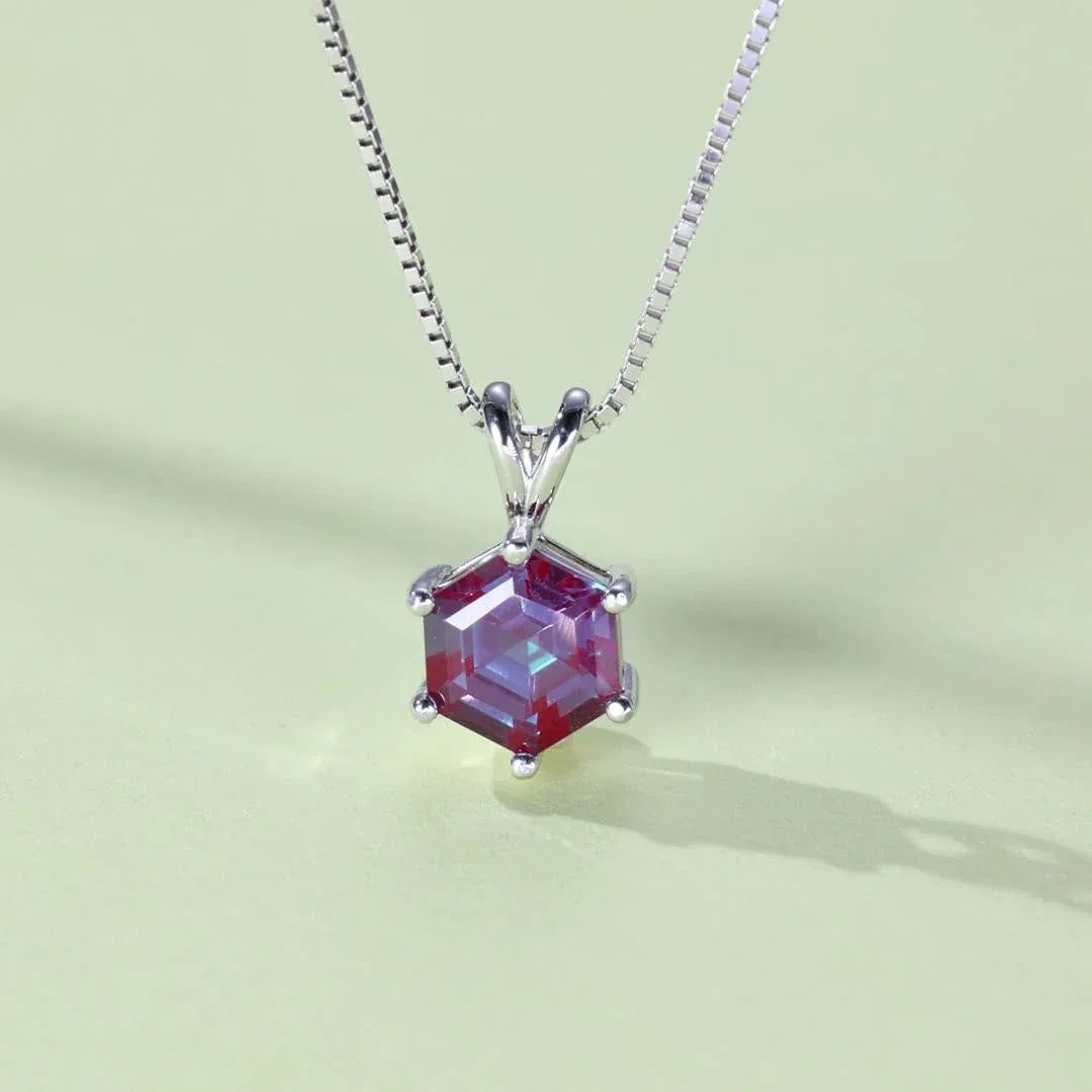 Hexagon Alexandrite pendant necklace with a three-bar bail, angled product view on a colored background