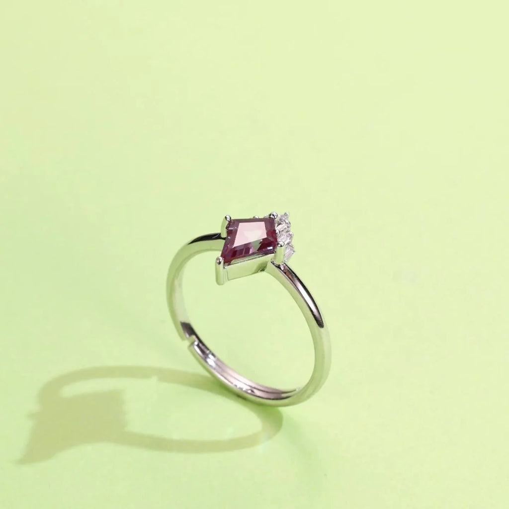 Kite-cut Alexandrite ring with a clear drop accent, angled product view on a colored background