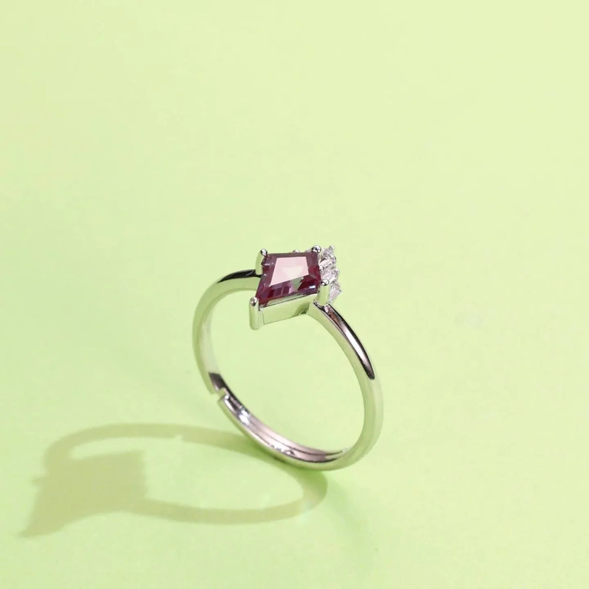 Kite-cut Alexandrite ring with a clear drop accent, angled product view on a colored background