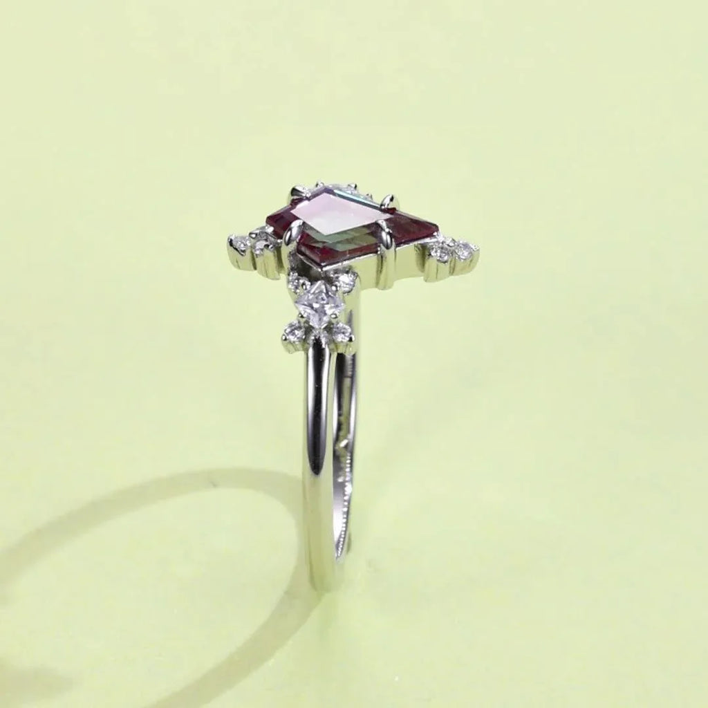 Kite-cut Alexandrite ring with clear halo accents, angled product view on a colored background