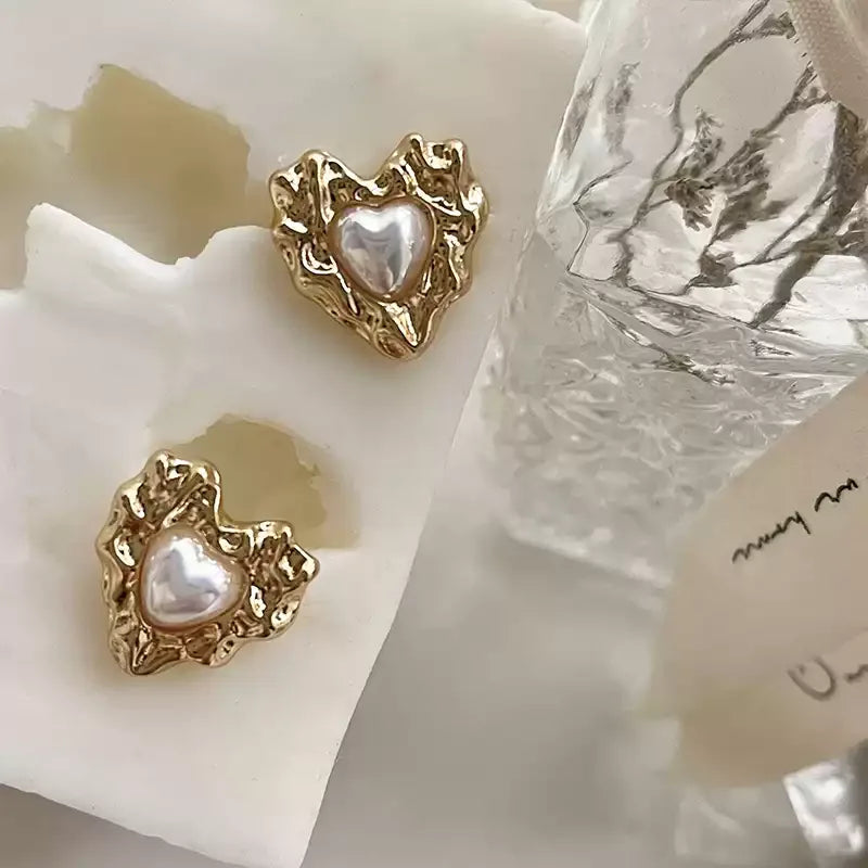 Molten-Texture Heart Pearl Stud Earrings — earrings displayed on a cream sculptural surface