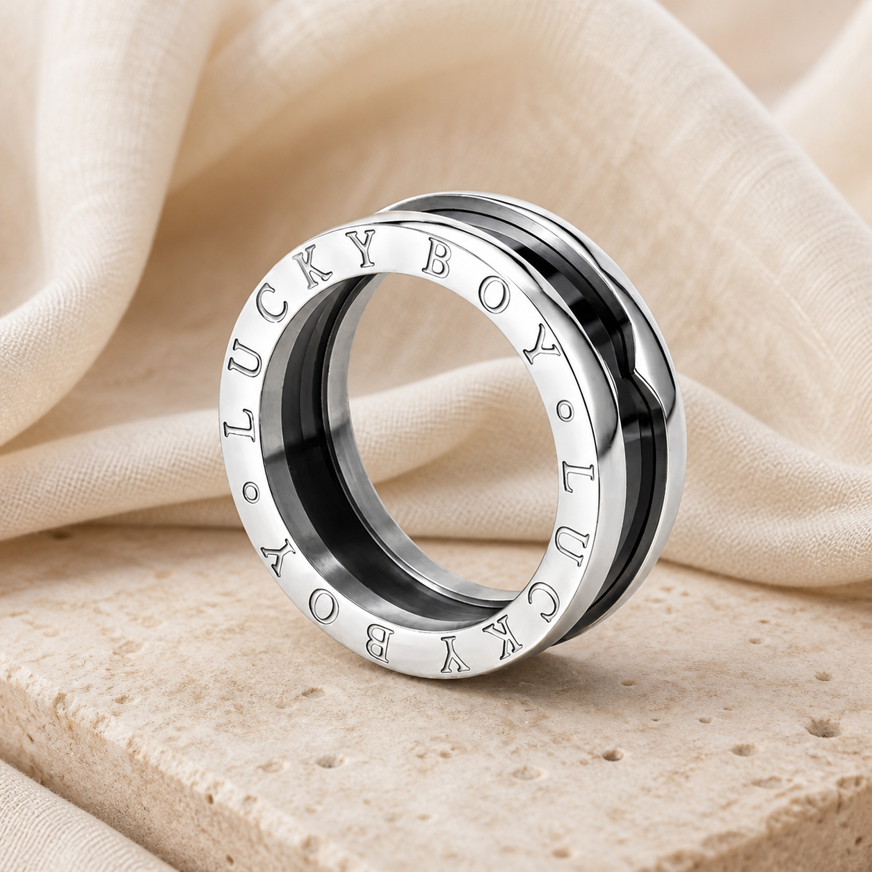 Silver and black spinner-style ring engraved LUCKY BOY displayed on warm beige stone