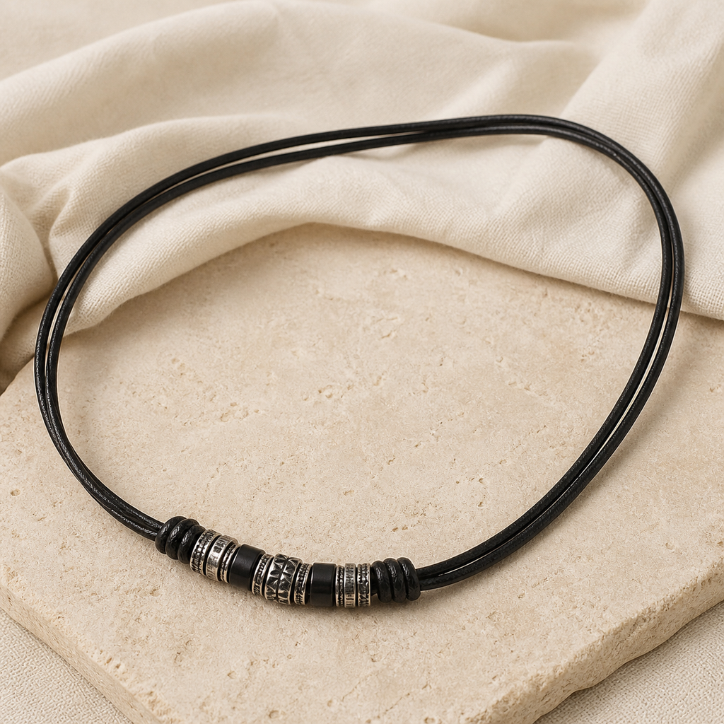 Black double-cord leather necklace with dark and engraved silver-tone beads on warm beige stone