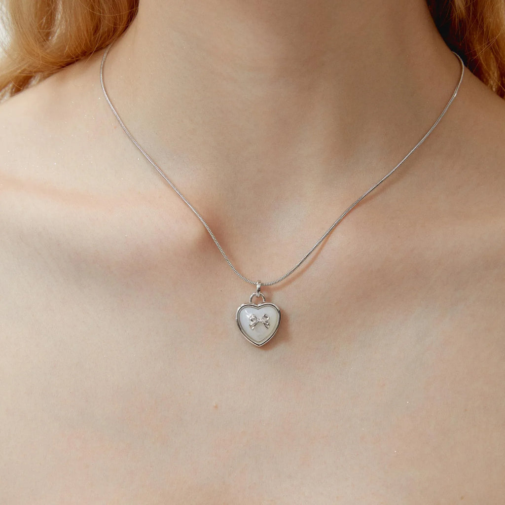 Pearl Heart Pendant Necklace with Bow Detail — neckline-worn close-up showing the pendant scale