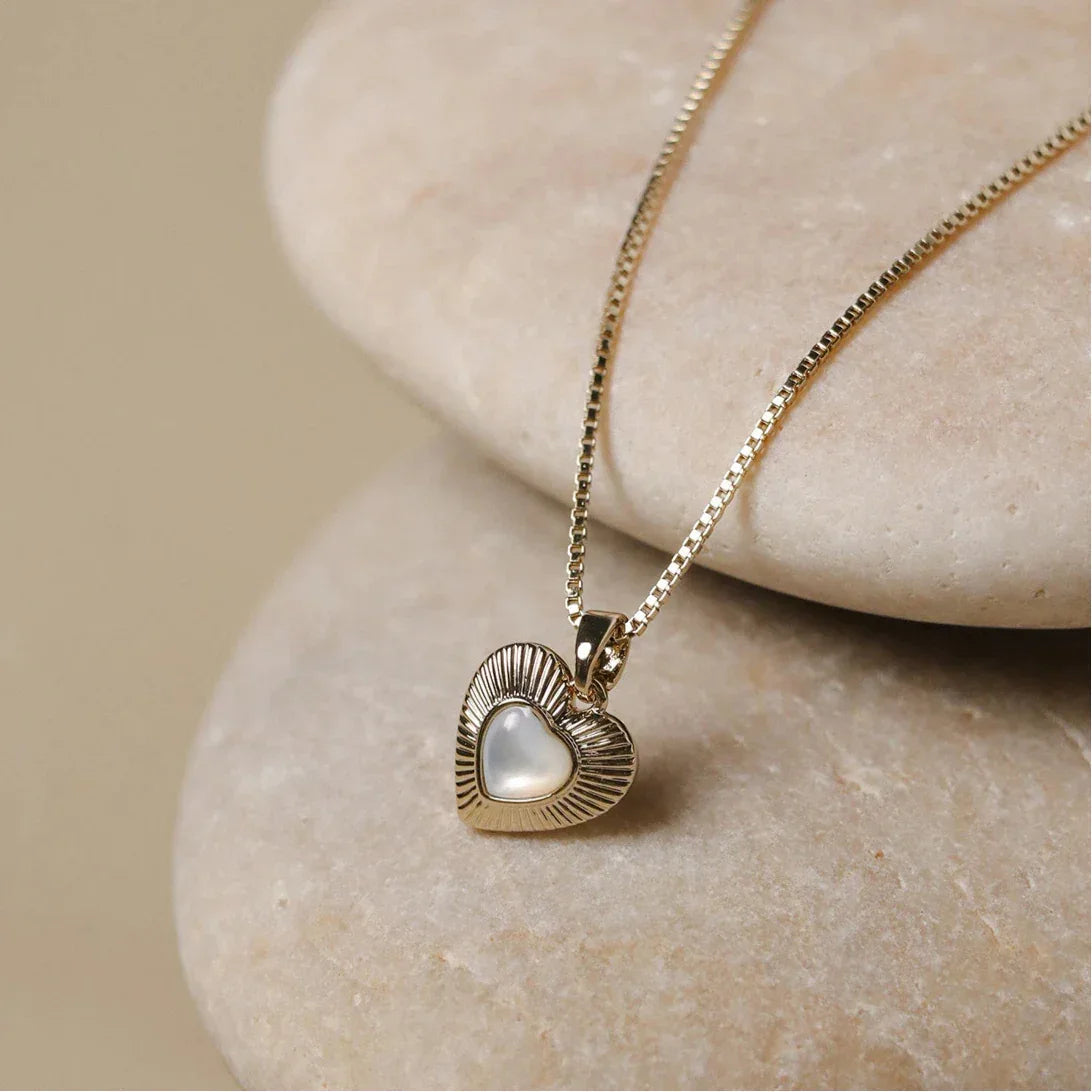 Ridged Pearl Heart Pendant Necklace — necklace arranged on a pale stone surface