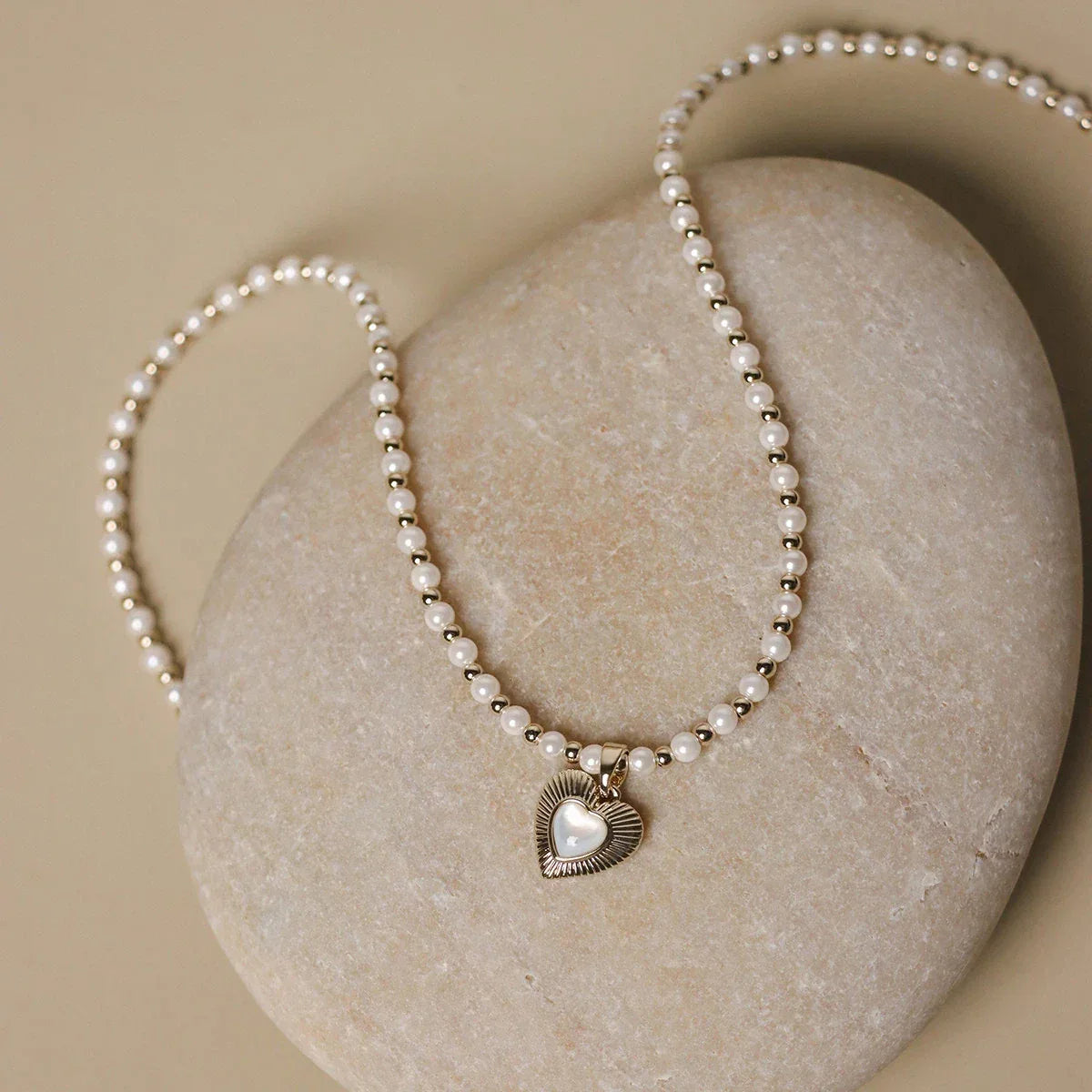 Pearl Bead Necklace with Petite Ridged Heart — necklace coiled on a pale display surface