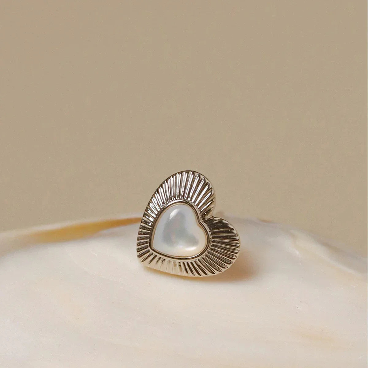 Petite Ridged Pearl Heart Stud Earrings — single earring displayed on a pale round surface