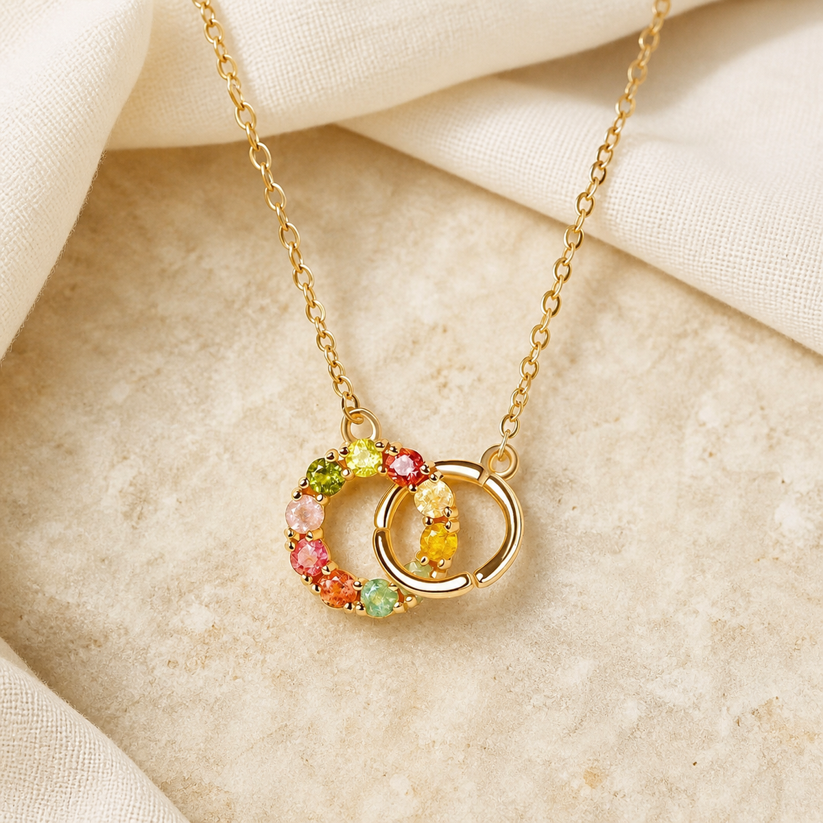 Gold-tone linked-circle pendant necklace with multicolor stones on beige fabric