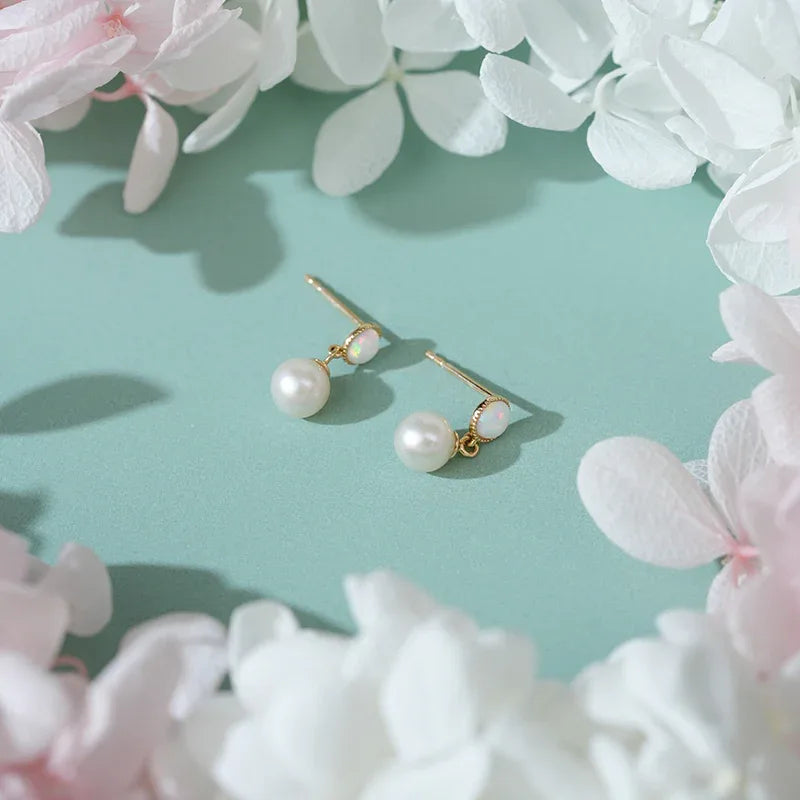 White Opal and Pearl Drop Earrings — pair laid among white flowers on a pale green surface