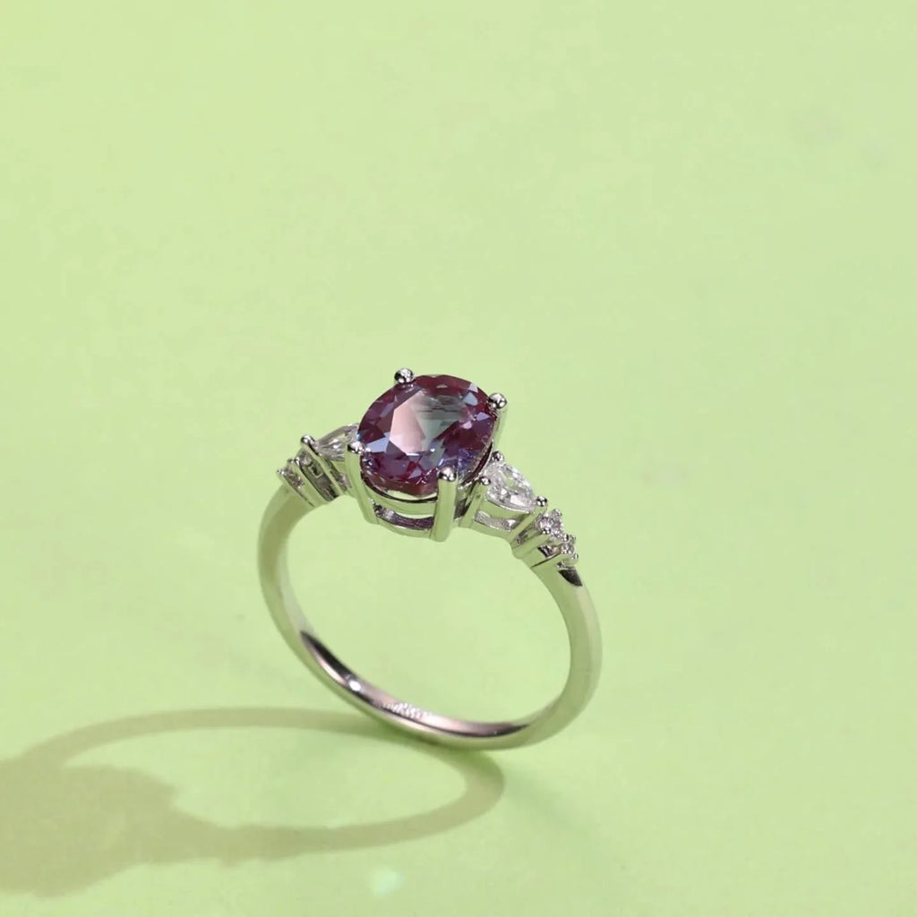 Oval Alexandrite leaf bypass ring with clear accents, angled product view on a colored background