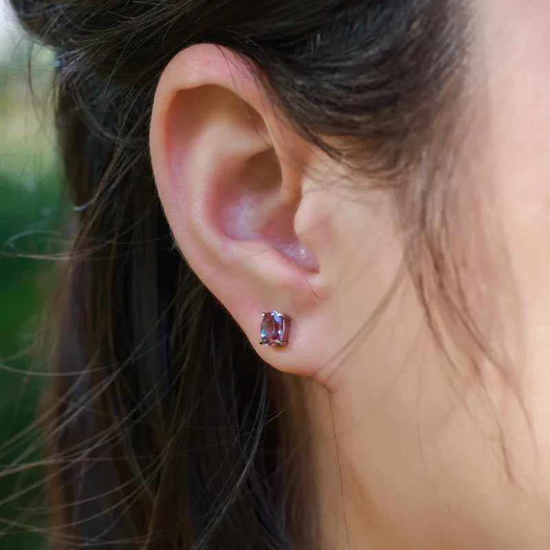 Oval Alexandrite stud earrings, shown worn on an ear for scale