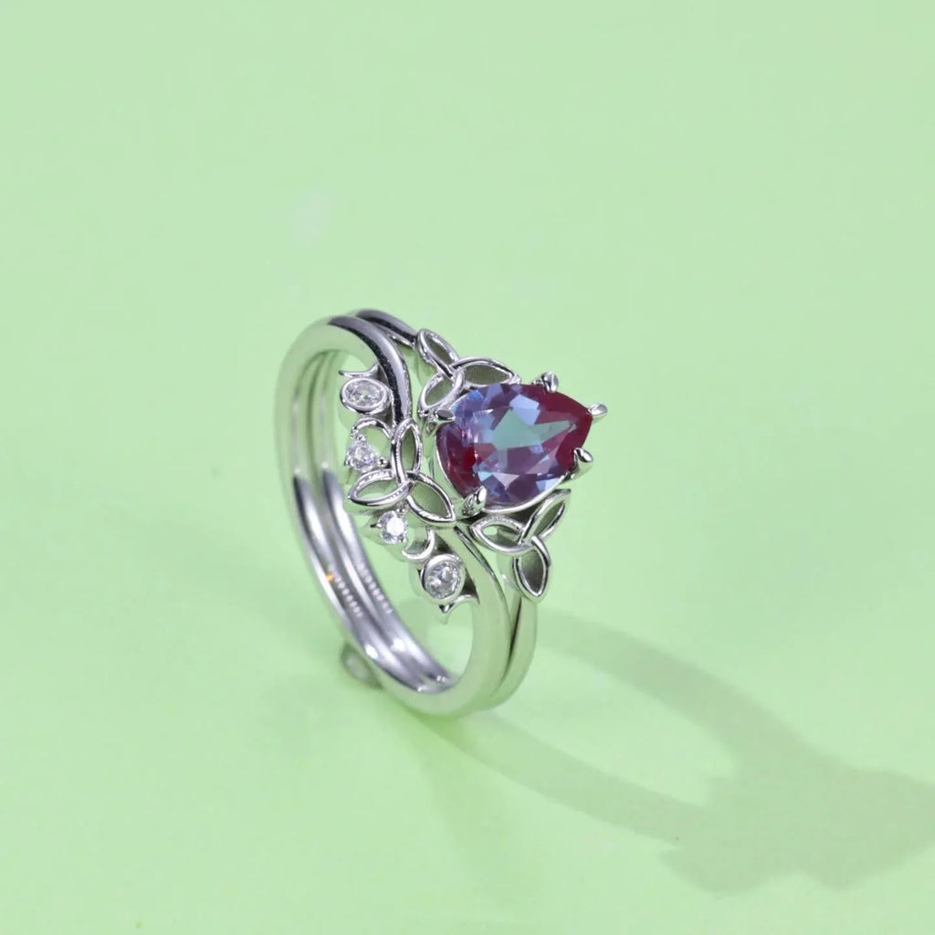 Oval Alexandrite three-band ring with leaf and clear-stone accents, angled product view on a colored background