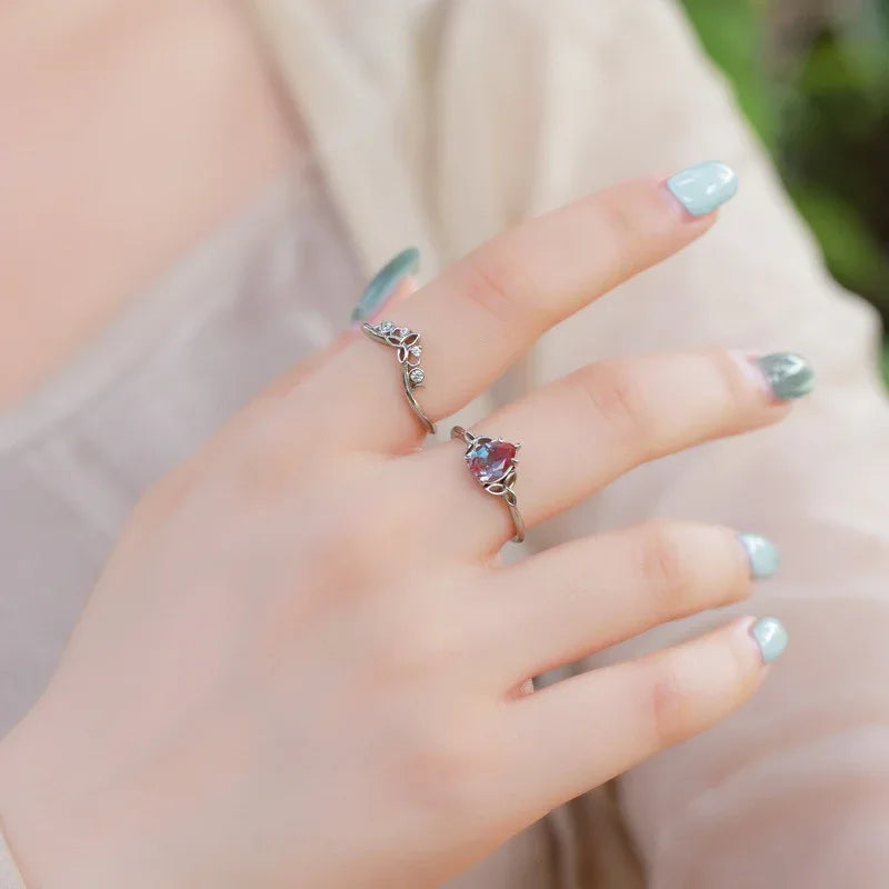 Oval Alexandrite three-band ring with leaf and clear-stone accents, shown worn in a close lifestyle view