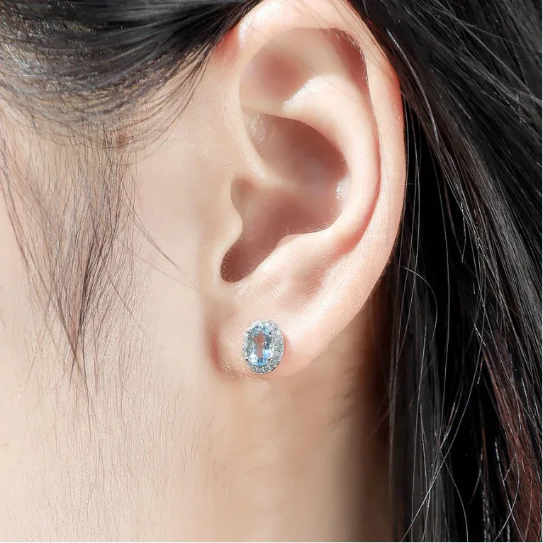 Oval Aquamarine Halo Stud Earrings worn on the ear in a close-up