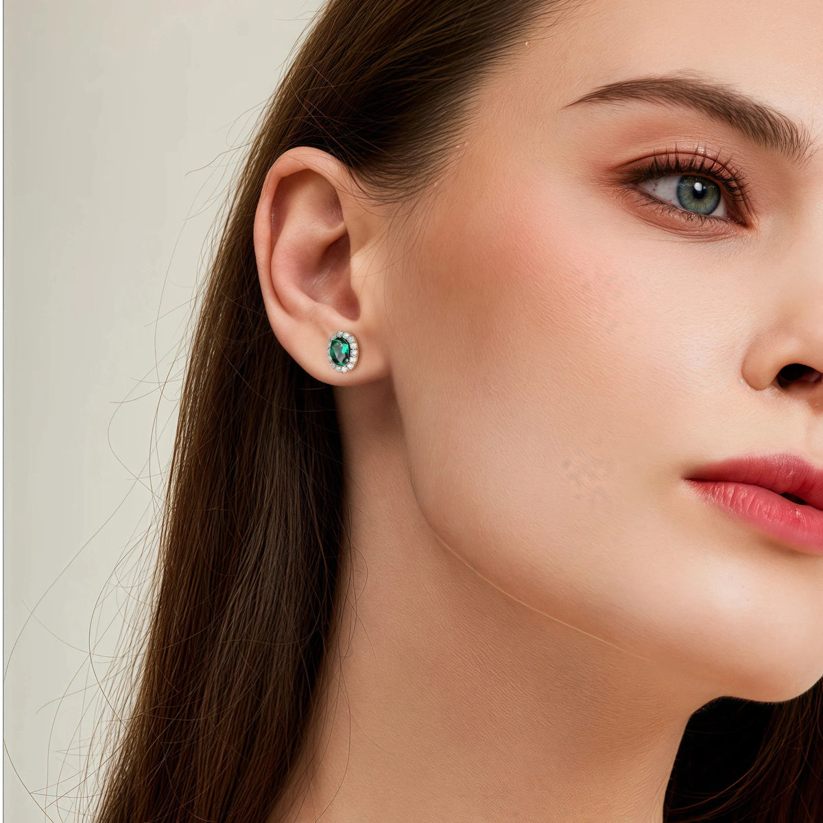 Oval Emerald Halo Stud Earrings worn on the ear in a close-up