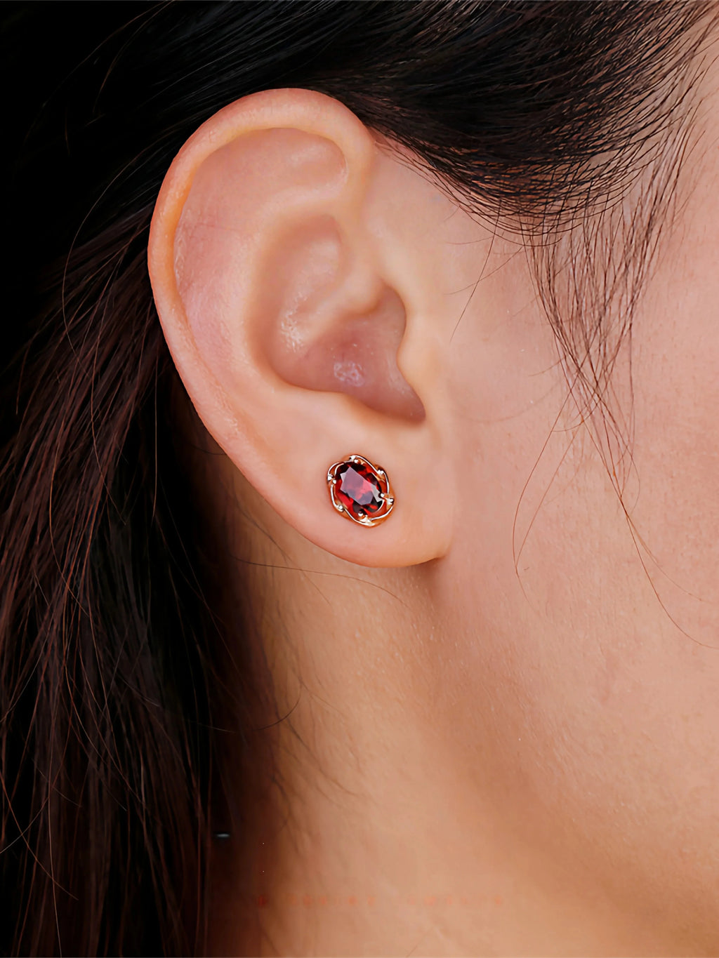 Oval Garnet Bezel Stud Earrings worn on the hand in a close-up