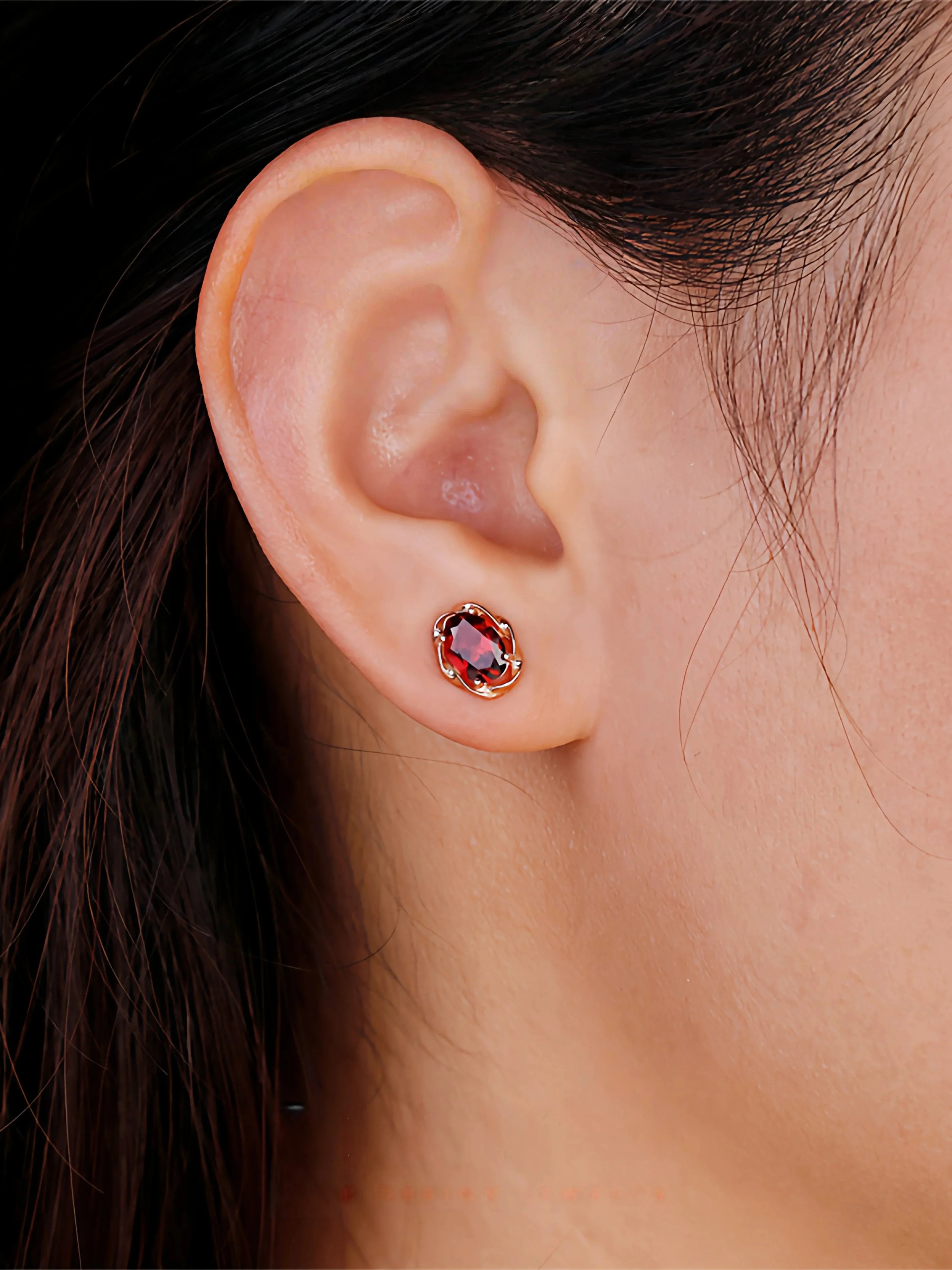 Oval Garnet Bezel Stud Earrings worn on the hand in a close-up