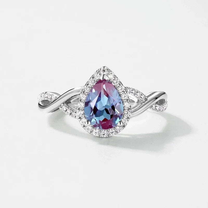 Pear-cut Alexandrite halo ring with a sweeping bypass band, center stone close-up on a white background