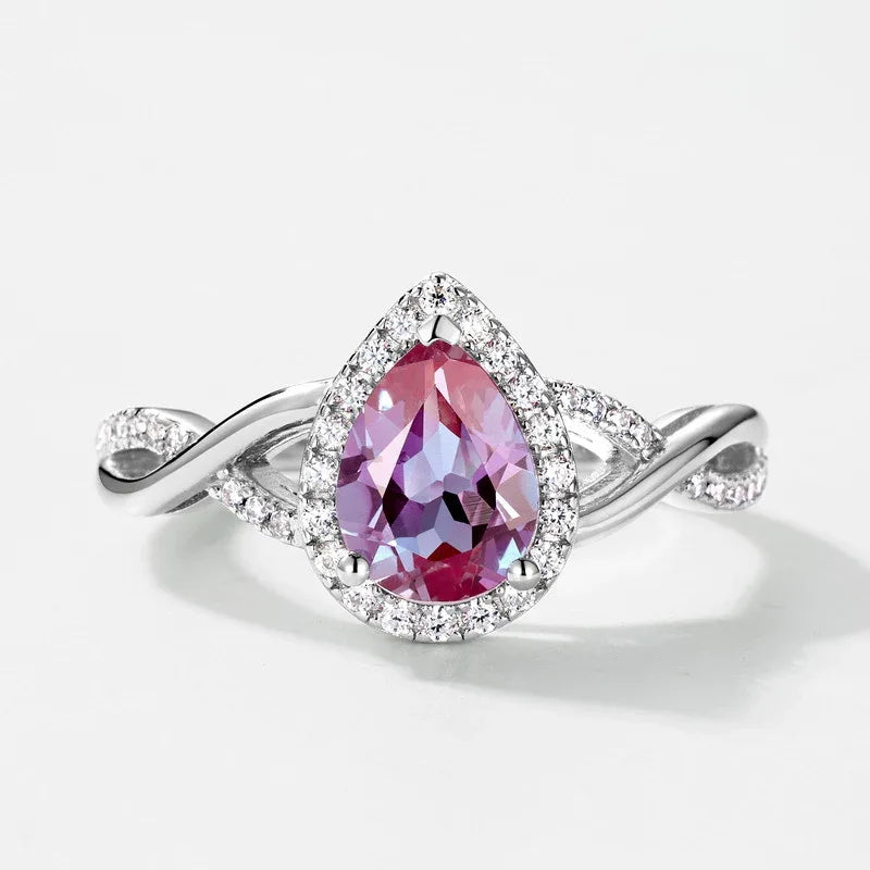 Pear-cut Alexandrite halo ring with a sweeping bypass band, pink-toned Alexandrite view under alternate lighting