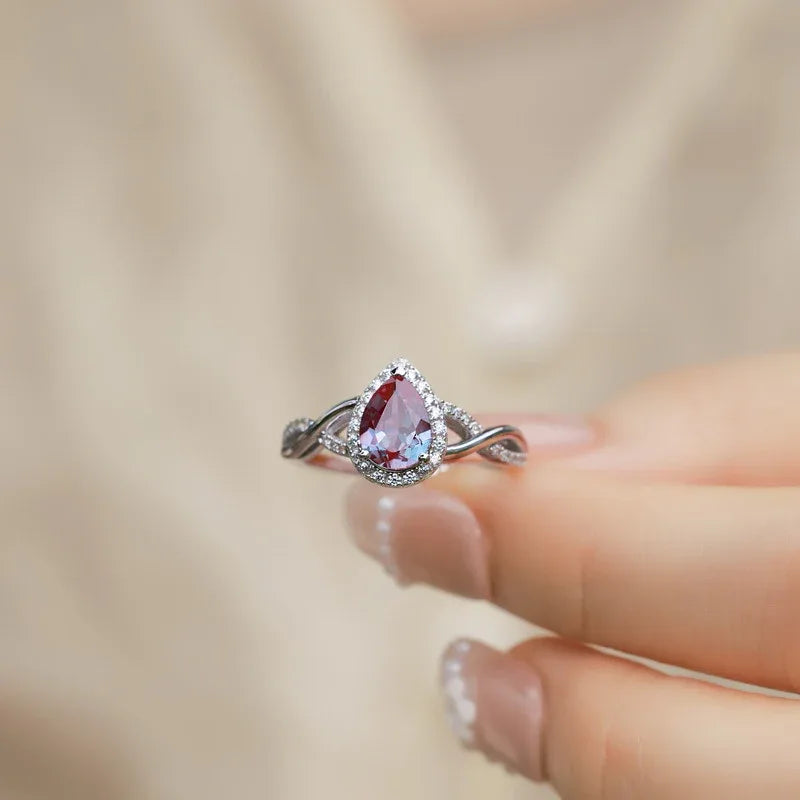 Pear-cut Alexandrite halo ring with a sweeping bypass band, shown worn in a close lifestyle view