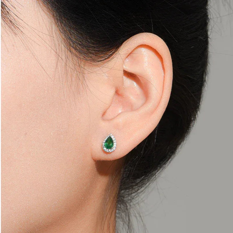 Pear-Cut Emerald Halo Stud Earrings worn on the ear in a close-up