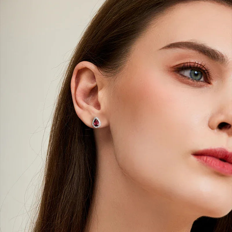 Pear-Cut Garnet Halo Stud Earrings worn on the hand in a close-up